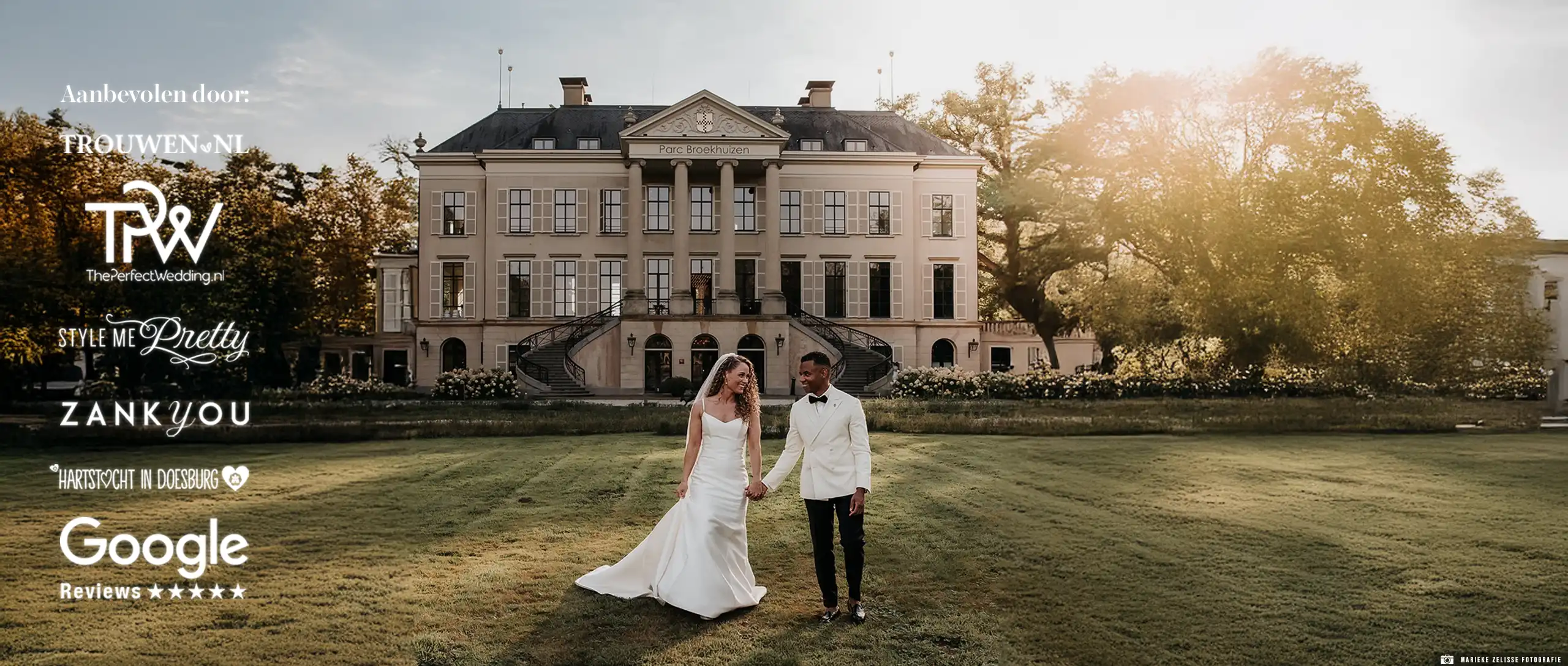 Een man in een witte smoking met een zwarte pantalon naast zijn bruid in een witte jurk op een grasveld.