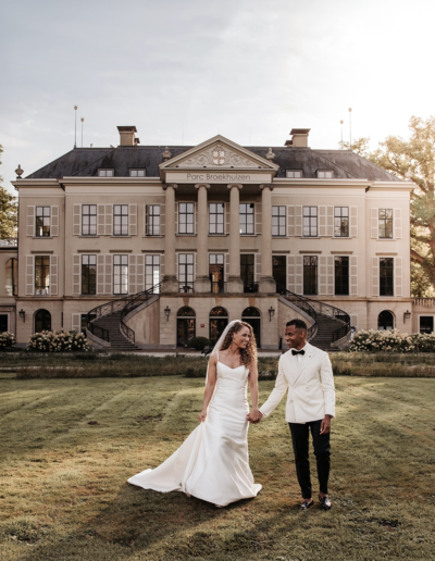 een bruidspaar in een witte smoking met een zwarte pantalon en een bruid in een witte jurk.